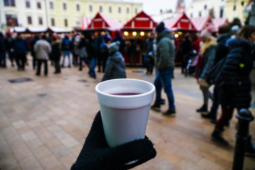 Hand colding a cup of wine in a Bratislava Christmas market, wearing gloves and using a styrofoam cup to hold read wine.