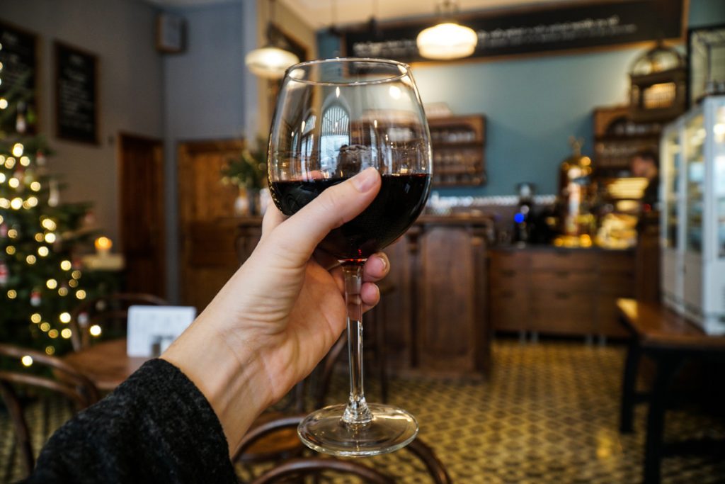 Hand indoors holding a glass of red wine with a Christmas tree visible nearby.