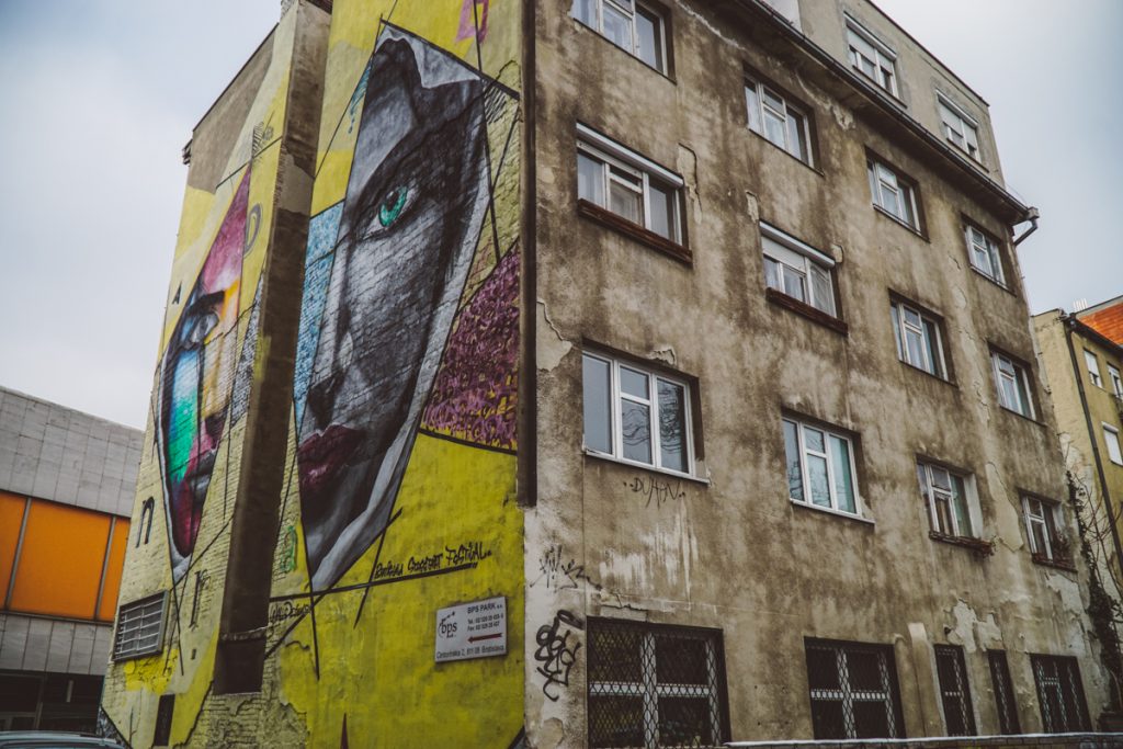 A slightly grungy building with a large yellow street art piece on the side of the building