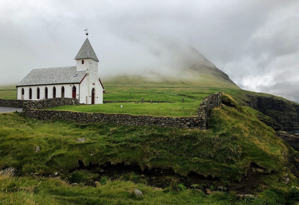 a silver-roofed church next to a green grass graveyard on a very foggy day