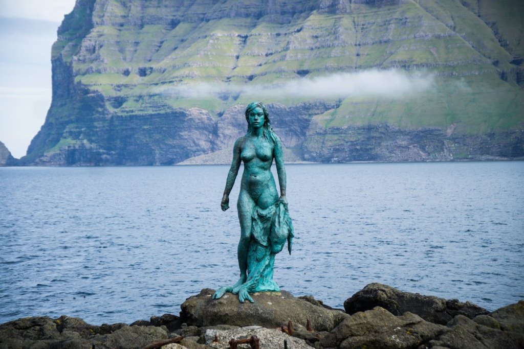 greenish blue patina covering a bronze sculpture of an unclothed woman in front of the sea