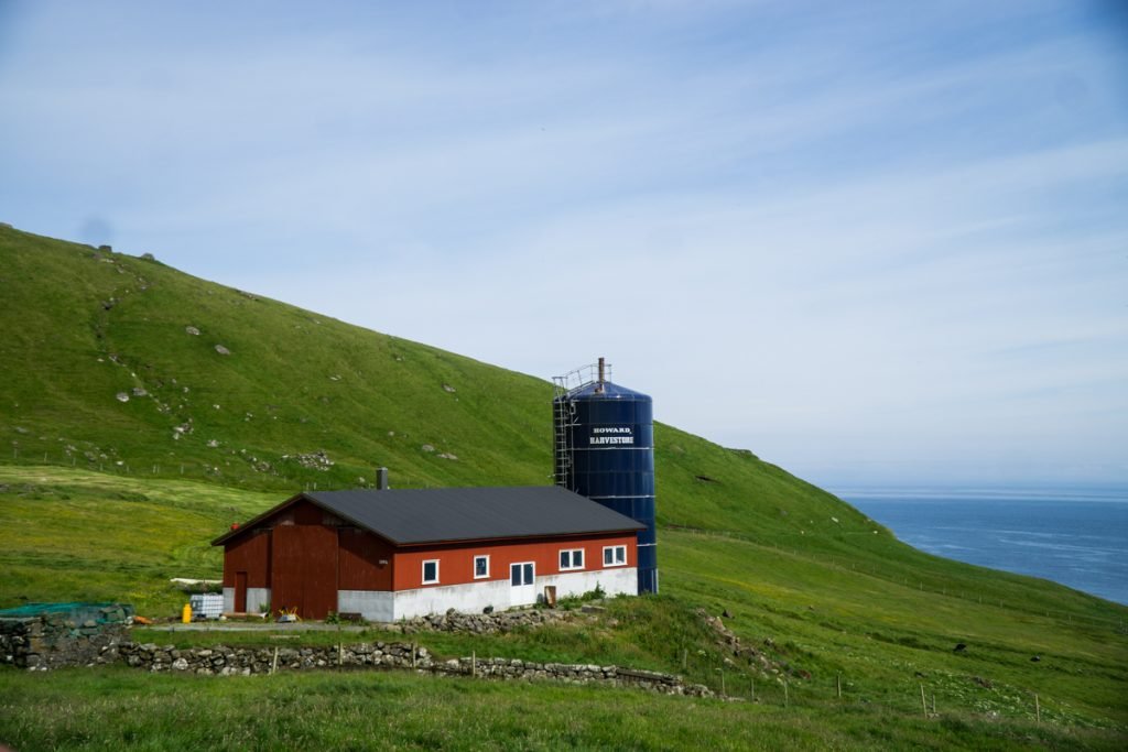 red building with a blue silo next to the trailhead for a popular hike in the faroe islands