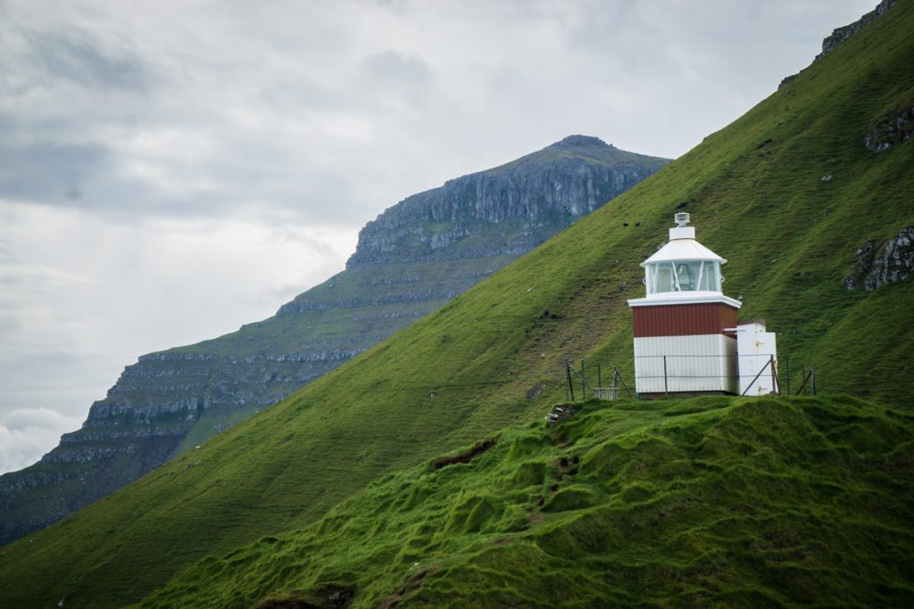 red and white lighthouse with rocky jagged cliffs nearby