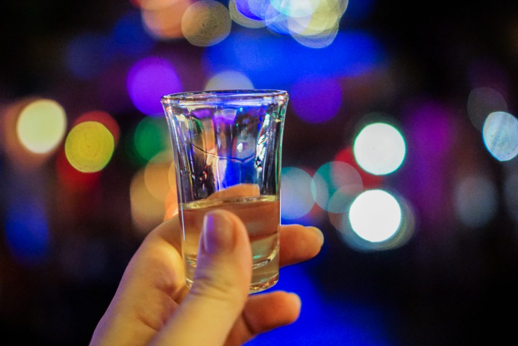 Allison's hand holding a glass of palinka at a Budapest ruin bar