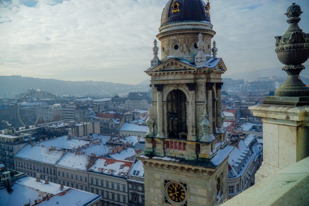 View during the day from the rooftop of the Basilica in Budapest, looking onto snow-covered rooftops, a Ferris wheel, and the Budapest skyline.