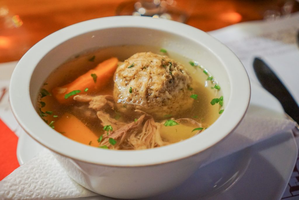 A bowl of matzo ball soup in Budapest with carrots and potato and meat, served with parsley, in a bowl in a Budapest restaurant in winter.