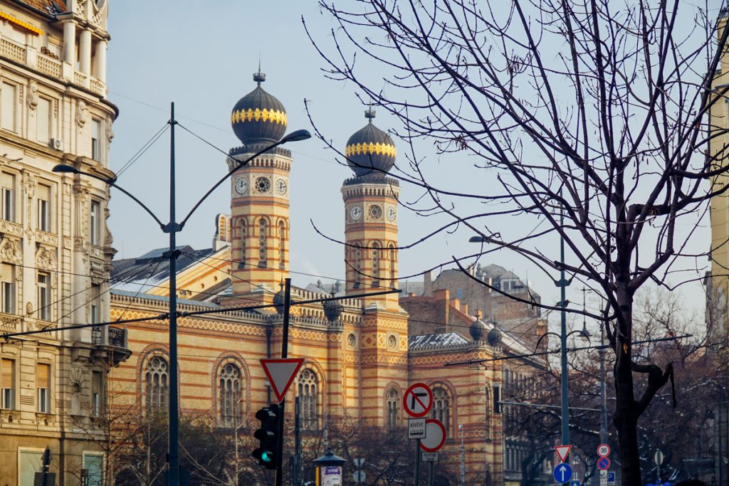 The exterior of the largest synagogue in Budapest with red stripes and golden domes and a clock on the tower.