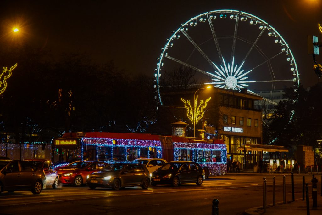 A festive lit-up Christmas tram in Budapest, with the Ferris wheel all lit up and also decorated behind it, showing the holiday spirit in Budapest in December.