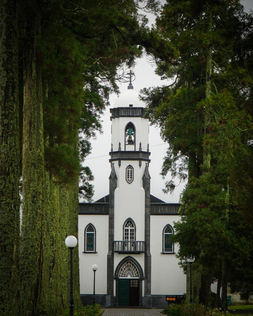 scenic white church surrounded by tall moss covered trees in sete cidades