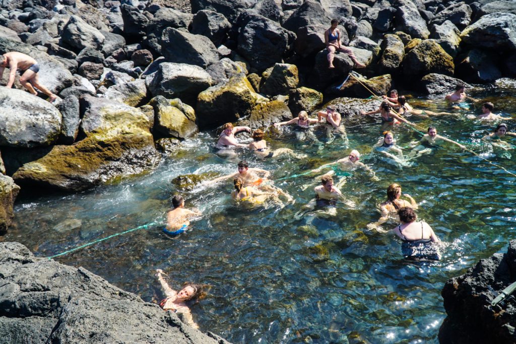 many people in the water with ropes enjoying the cool and hot waters of the ponta da ferraria