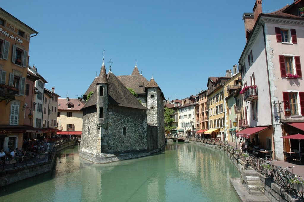 the famous canals of annecy with a beautiful castle-looking building with a turret in the middle of the canals in this medieval french village