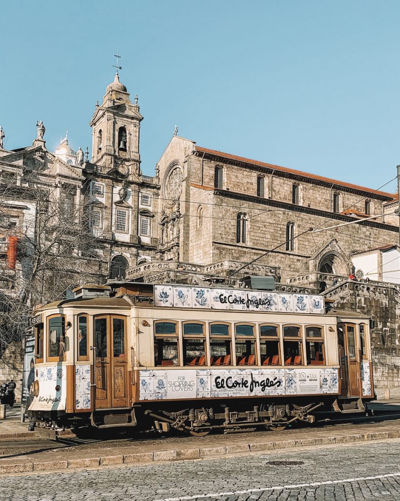 A tram in Porto in a scenic area of the city with azulejo-like design, advertising the El Corte Ingles department store