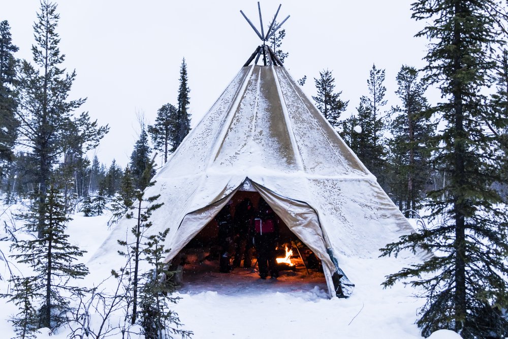 People around a fire inside a traditional Sami-style lavvo tent