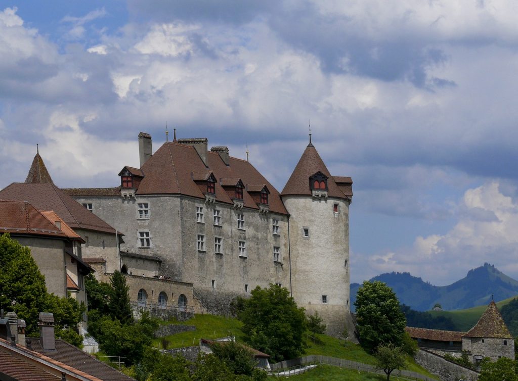 a giant swiss castle on a cloudy day with beautiful stonework and turrets and mountains in the distance