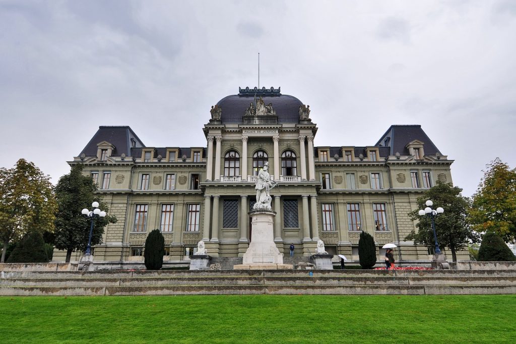 fancy building in lausanne on an overcast day with a statue in front of it and a green lawn