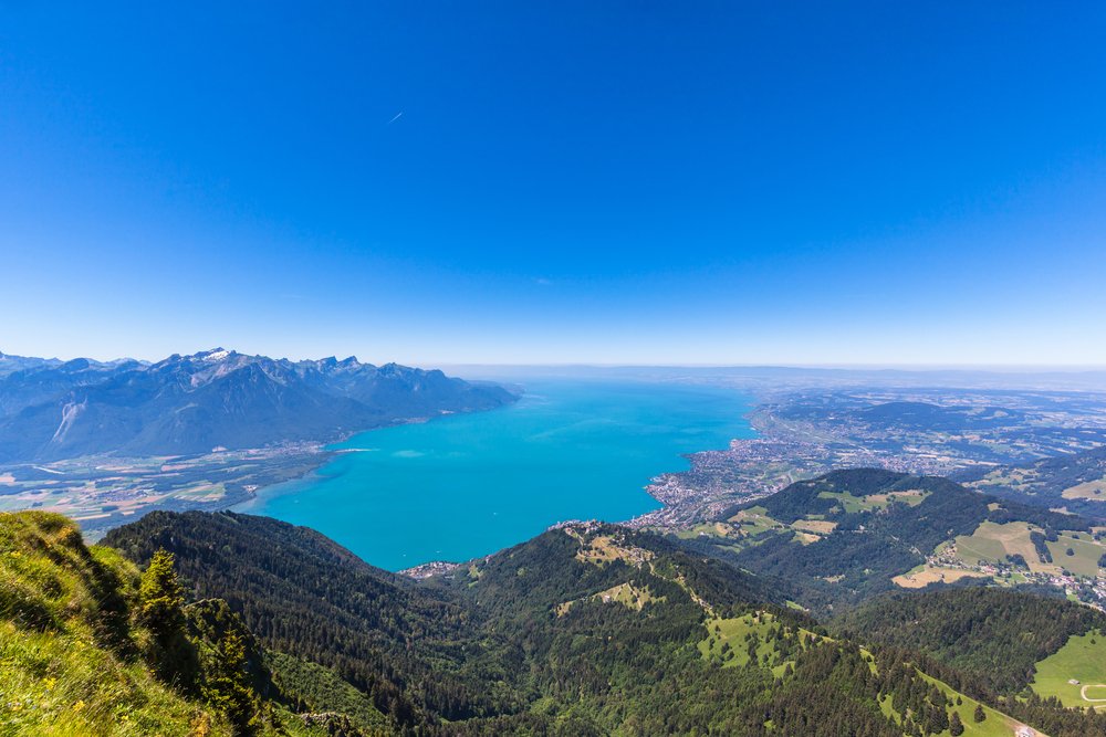 the brilliant blue of lake geneva as seen from high above on a mountain, views of small towns around the lakeshore