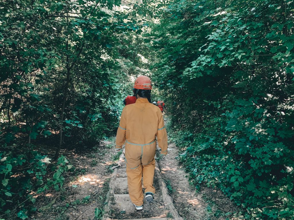 Someone in a yellow caving jumpsuit and an orange hard hat walking down the stairs towards the caving system in Budapest