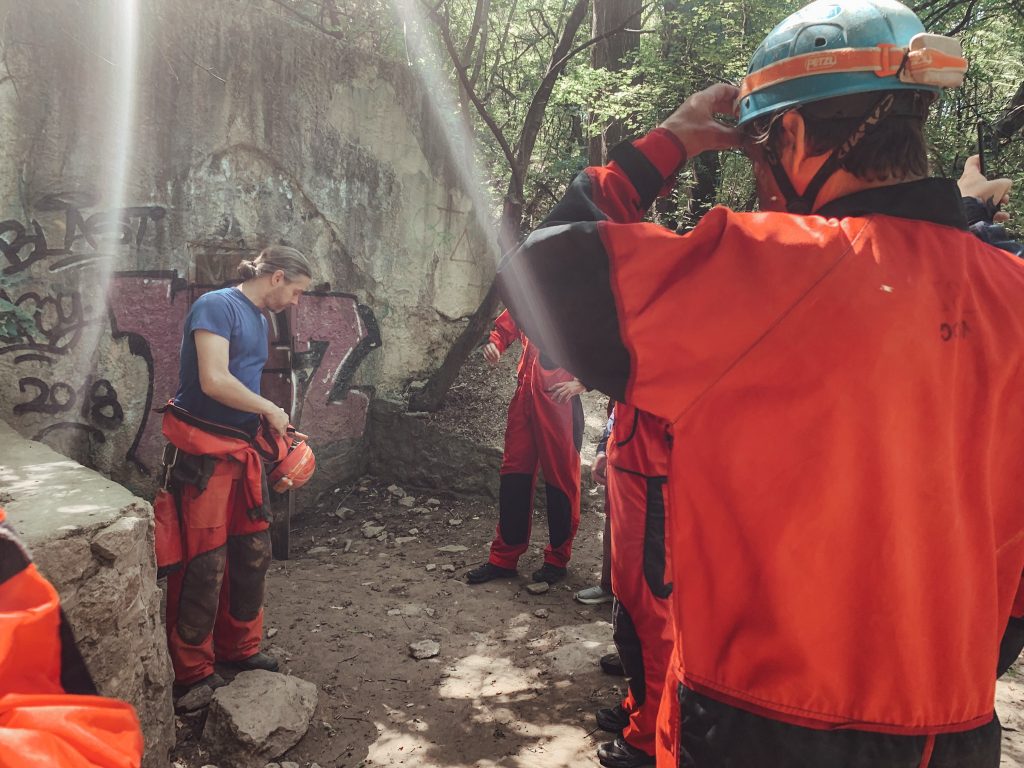 The cave tour guide gearing up, with people in orange caving jumpsuits and a blue hard hat, outside before the cave tour