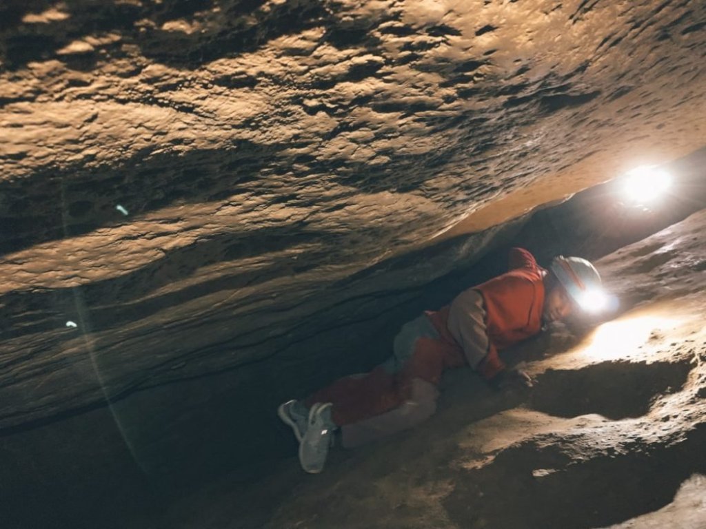 A person in an orange jumpsuit and blue hard hat squeezing through a crevice in the Budapest cave system