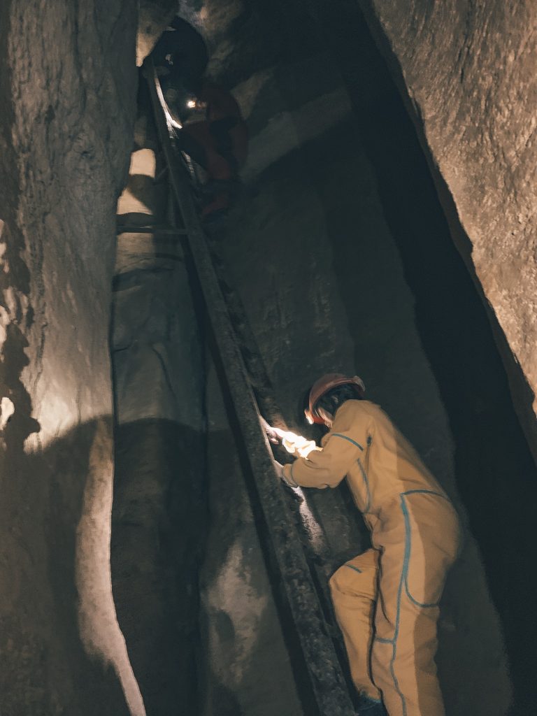 A person in a yellow jumpsuit going up a ladder at the end of the cave tour