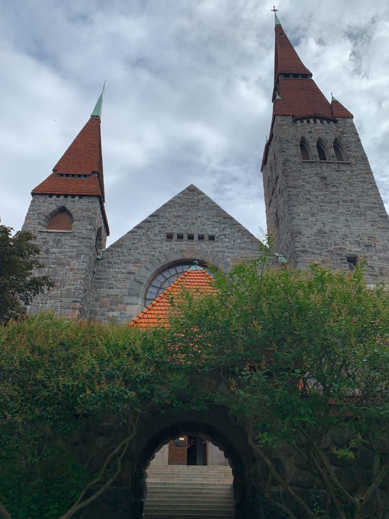 two steeples of a brick cathedral, different heights, with one tower higher, against a cloudy sky