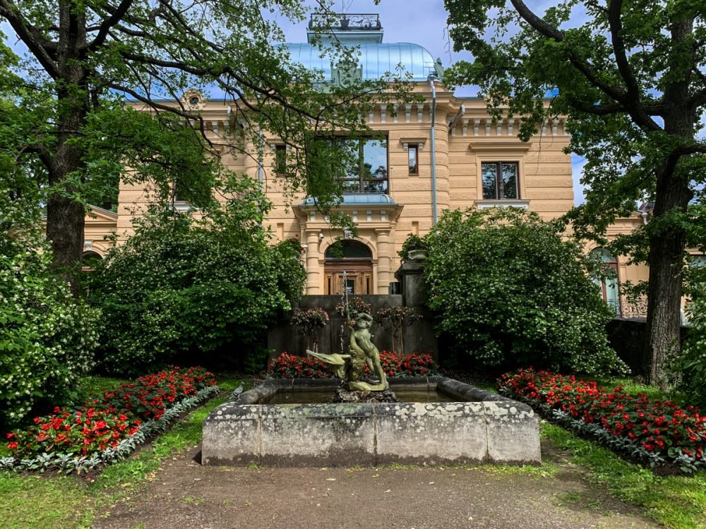 an ornate palace with a mermaid sculpture in front of it and summer flowers in red colors and white