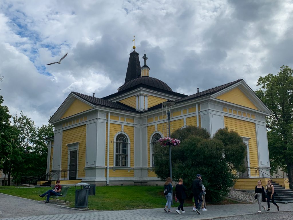 a bright yellow church with a gray or black roof against a cloudy sky