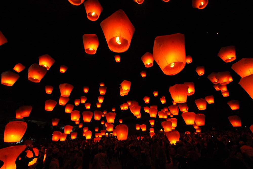 lit orange lanterns floating towards the sky, as seen from a low angle