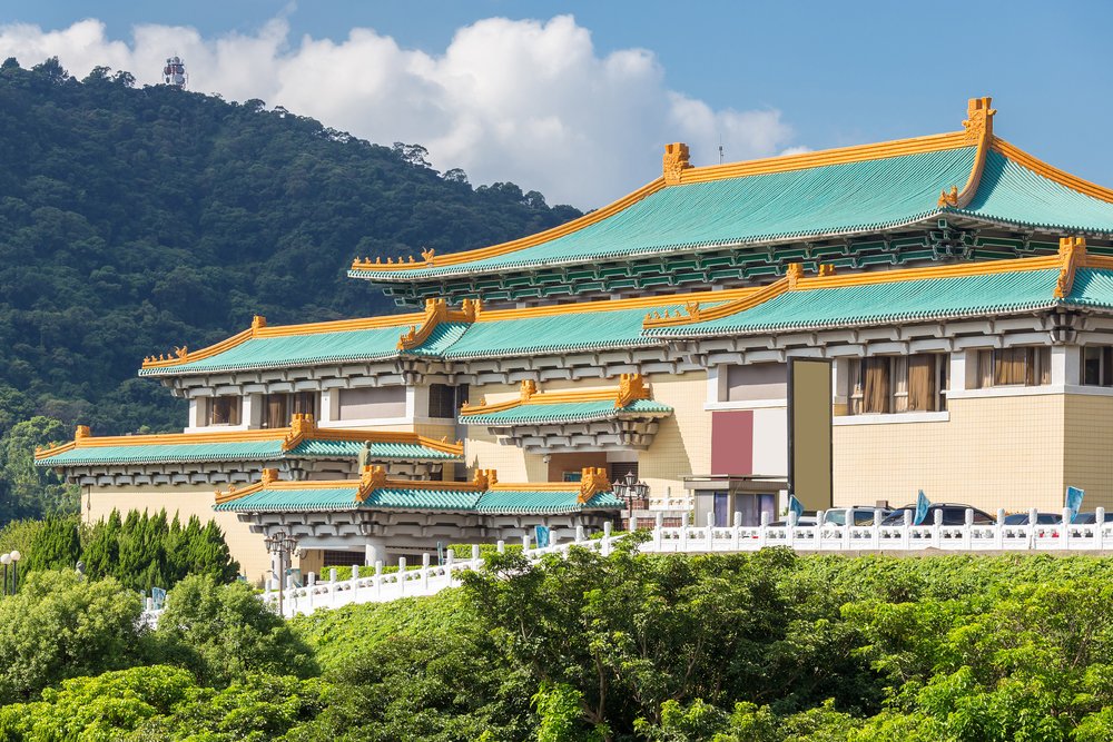 beautiful architecture of the national palace museum with teal green roof with gold accents, many tiers, with mountainous lush background.