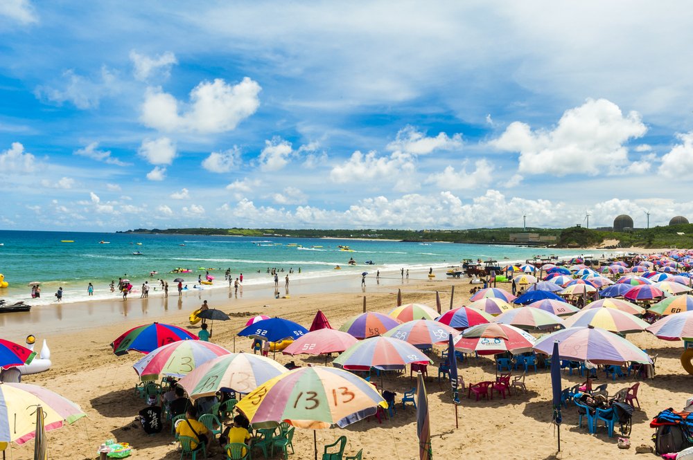 packed beach in the kenting area with rainbow colored umbrellas and lots of people enjoying holidays