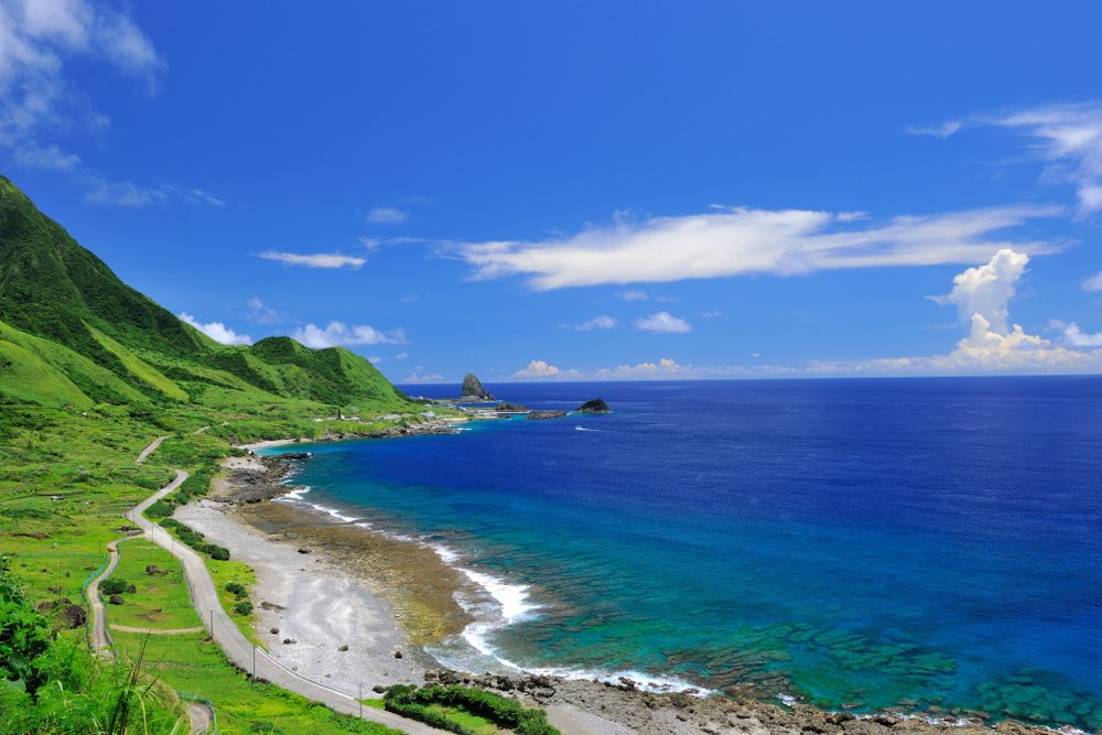 brilliant ocean waters in turquoise and dark blue meeting a sandy beach and green landscape