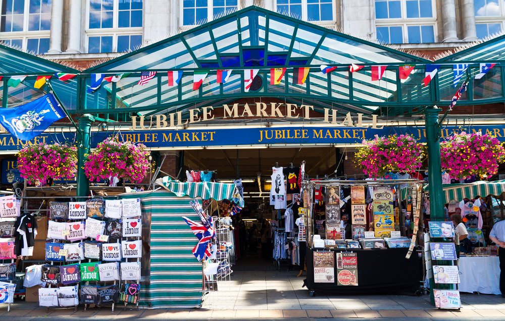 sign that reads jubilee market hall with baskets of pink flowers and things for sale outside