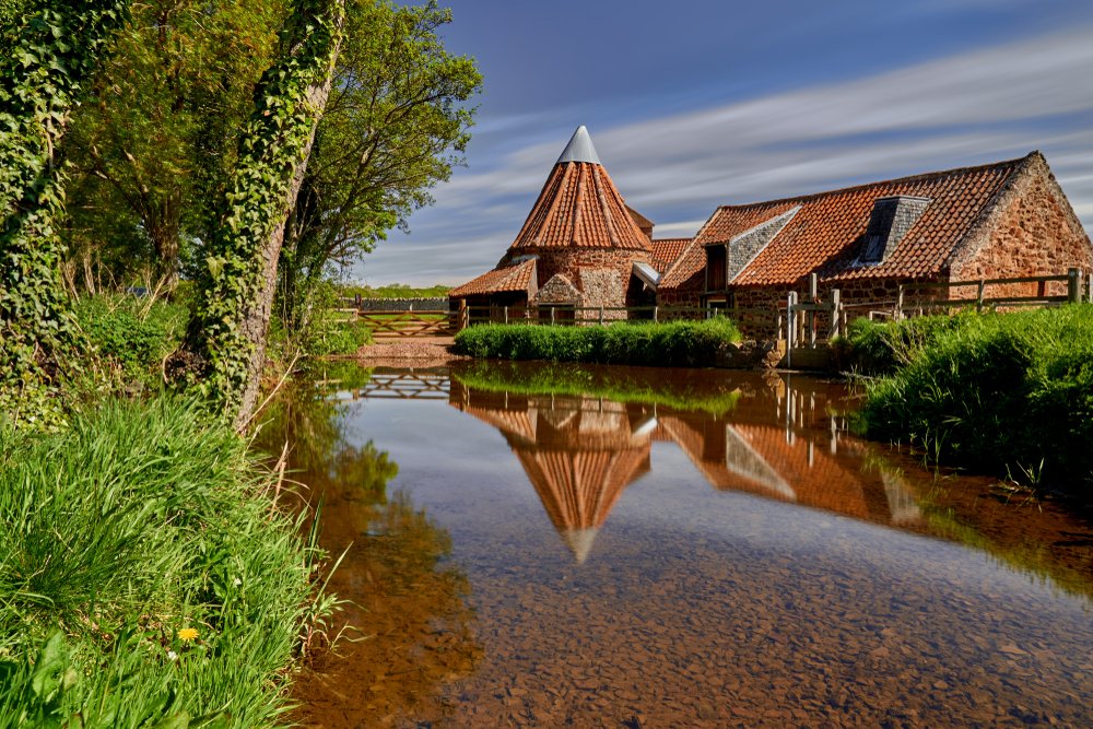 Still water, trees, blue sky, and an old watermill