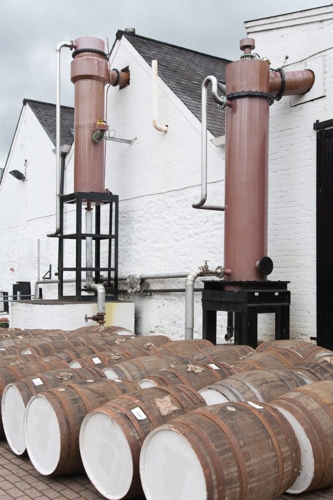 White distillery building with whiskey barrels outside