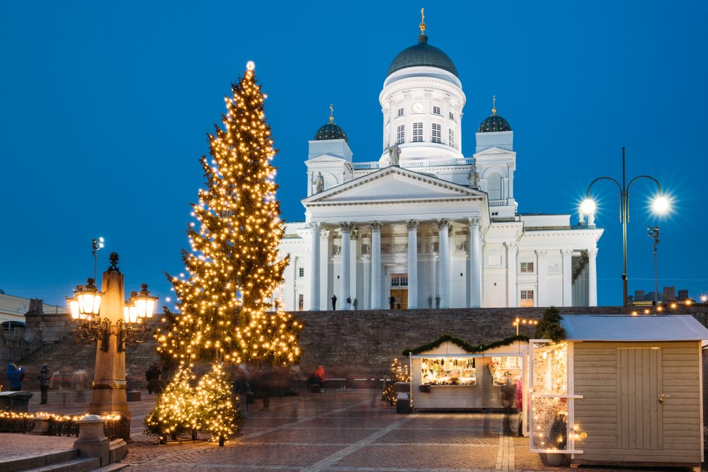 The white architectural facade of the Helsinki Cathedral with the Christmas tree lit up in front of it.