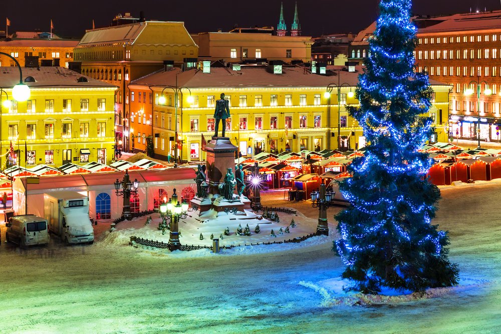 View of the Helsinki winter Christmas markets during the evening hours with gorgeous little red chalets and a Christmas tree.