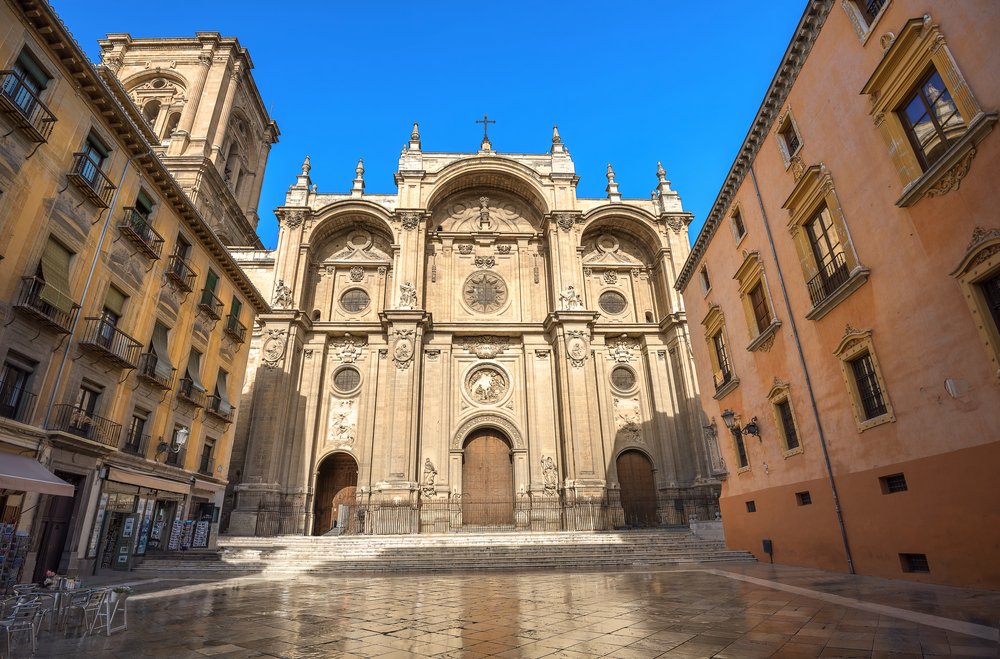 Famous face of the cathedral in Granada with historic buildings around it in the square