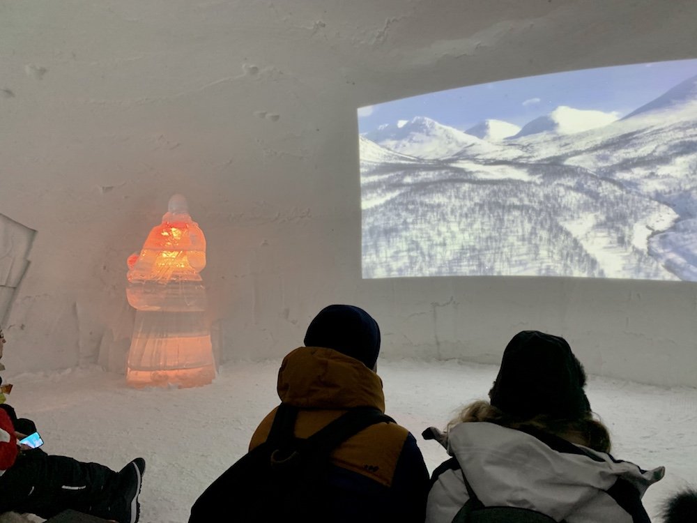 People sitting to watch a movie being projected on an ice wall showing how the Ice Domes are constructed each year
