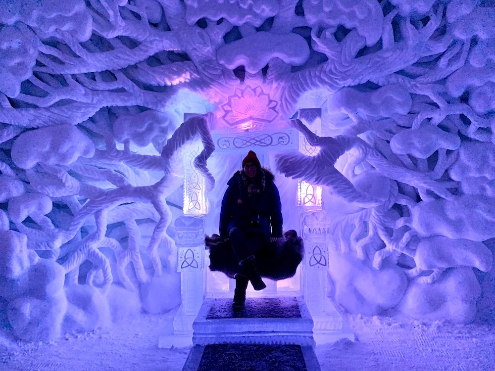 Allison wearing a warm jacket and sitting in a throne made of sculpted ice at a Norwegian ice hotel