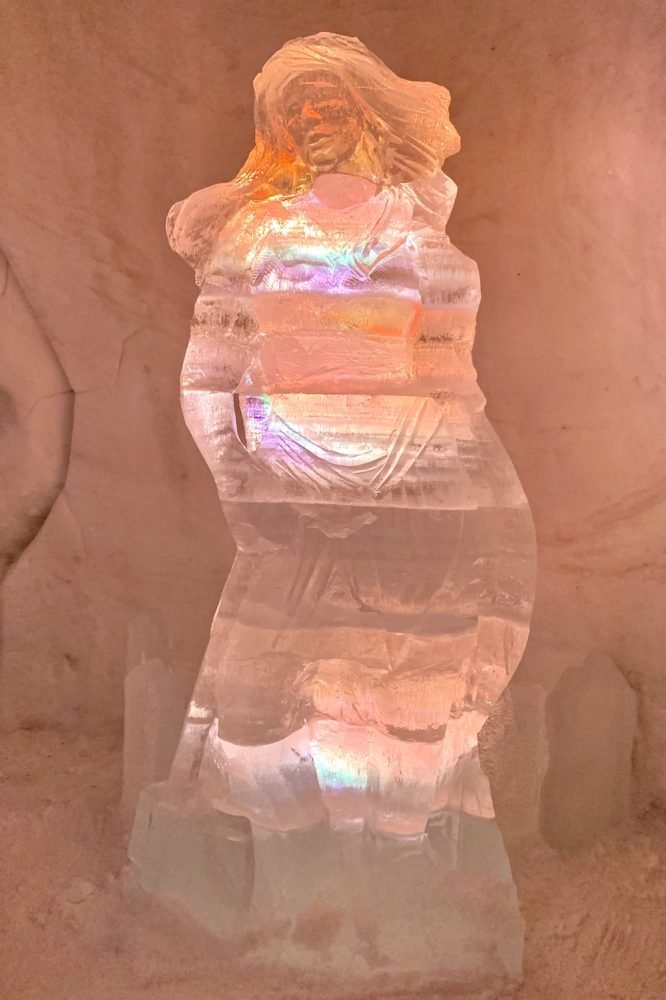 A sculpture of a woman made of ice inside the ice hotel with a soft orange lighting