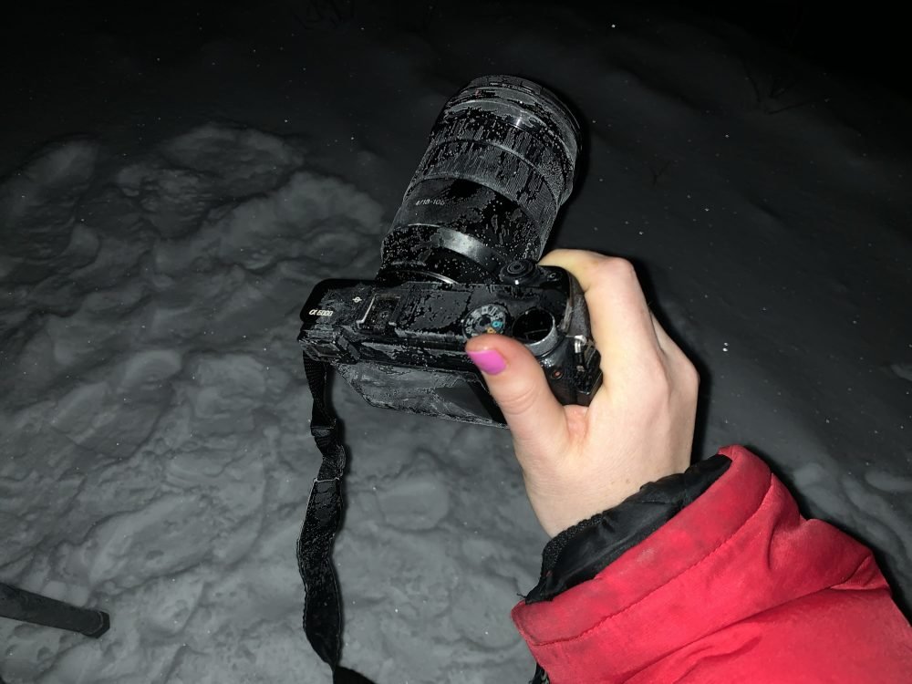 Allison's hand in a puffy jacket, while holding onto a camera that is very covered in ice crystals