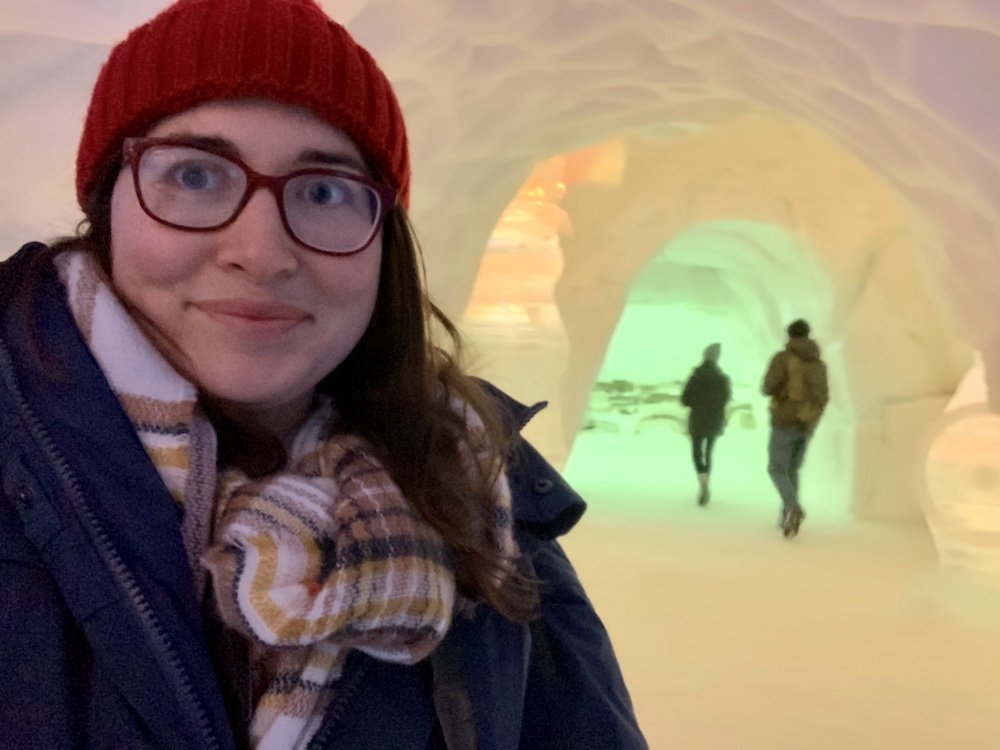 Allison Green smiling during a selfie at the Tromso Ice Domes, wearing glasses and a red hat and a winter coat.