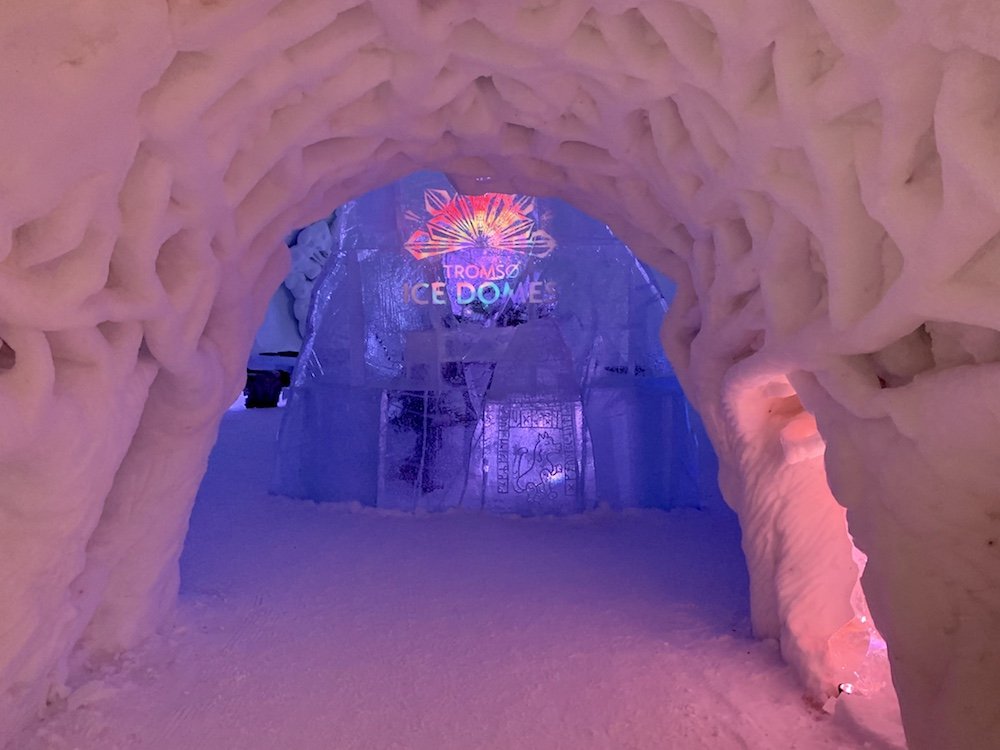 View of the interior of the Ice Domes, with a light display that says 'Tromso Ice domes' and pink, blue, and lavender lighting in the interior of the igloo.