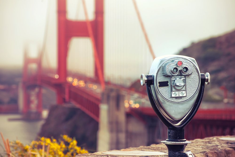 Pay-per-use viewfinder in focus with an out of focus background of the Golden Gate Bridge with cars on it on a foggy day.