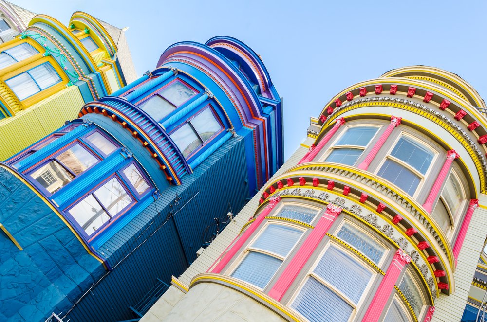 View from a low angle of the rounded, colorful, detailed buildings of San Francisco architecture: one yellow, one blue, and one pink-and-white building.