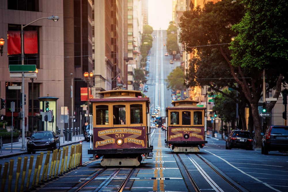 Two distinctive San Francisco red-and-gold cable cars passing each other on a busy city street with soft afternoon light.