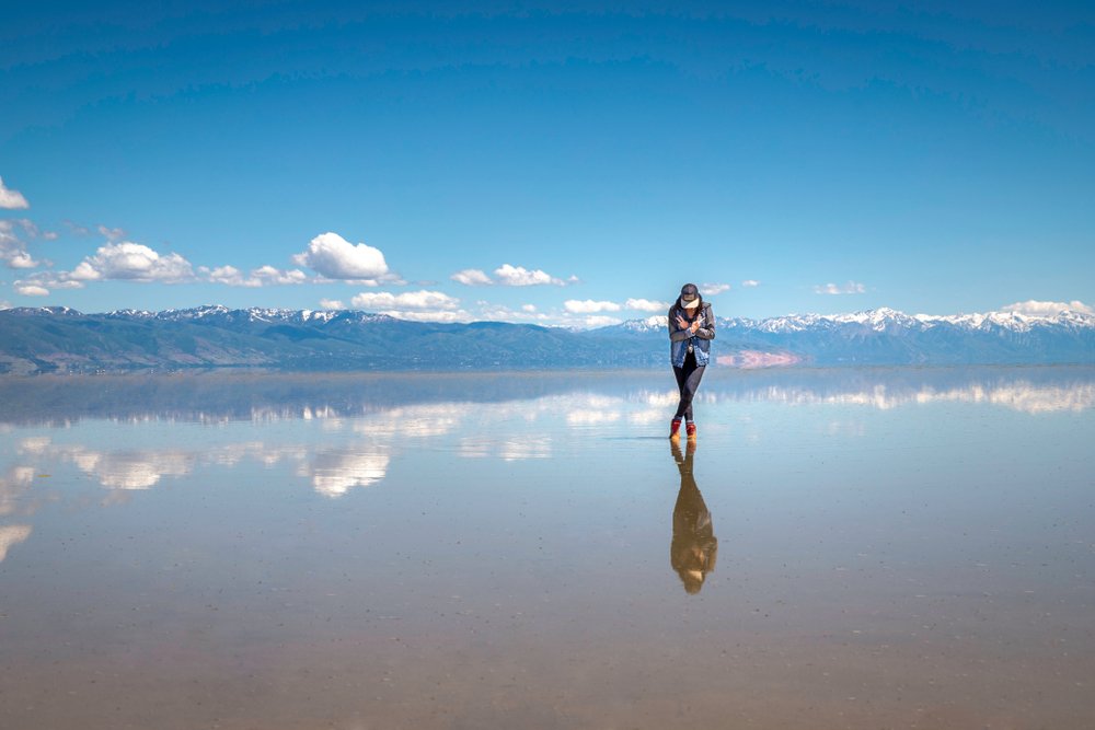 Woman standing on reflective salt lake with shallow water and clouds