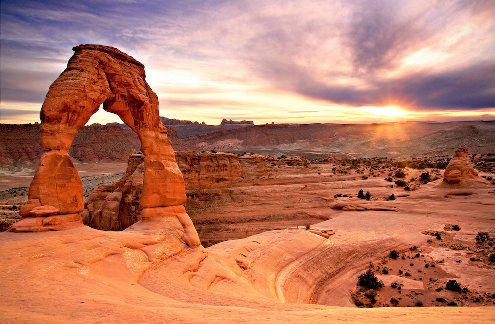 Delicate Arch thin stone arch shown at sunset with red rock background