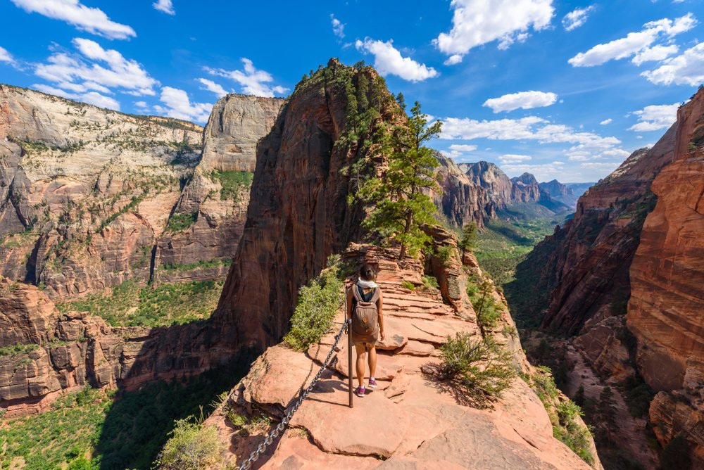 Woman hiking Angels Landing, a ridge hike with a chain assist, with views of the valley in Zion National Park on all sides.