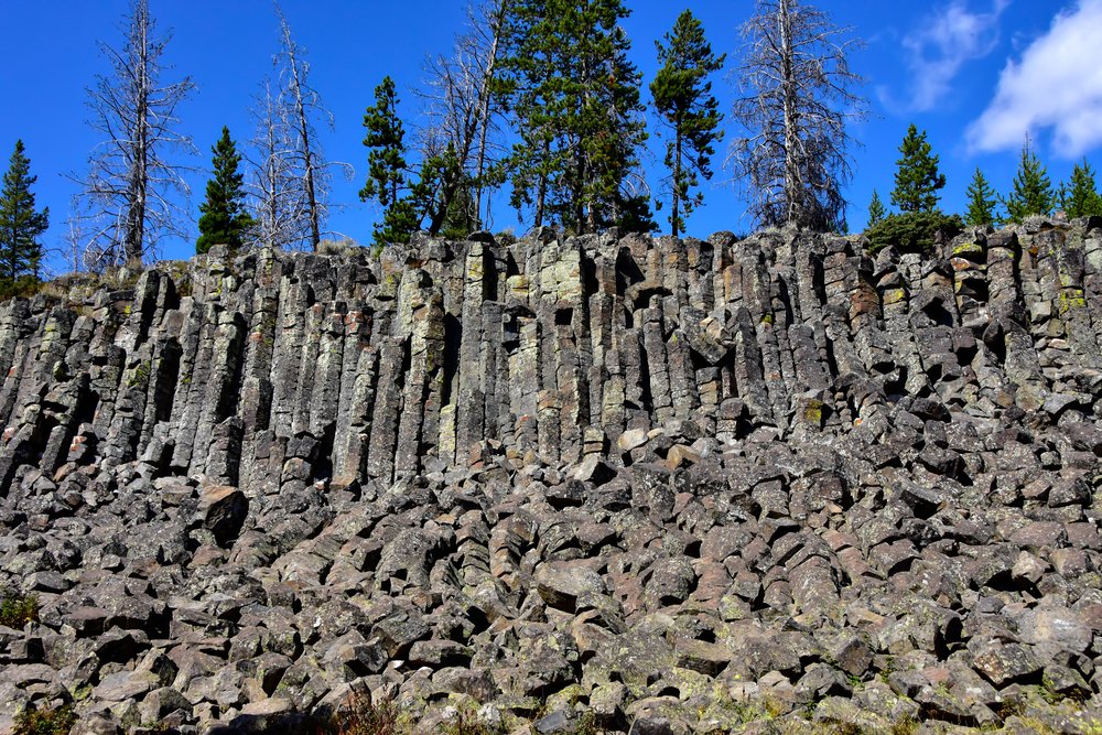 Gray basalt columns with lots of smaller, broken apart rocks at the base, on a sunny blue sky day with a patch of clouds.